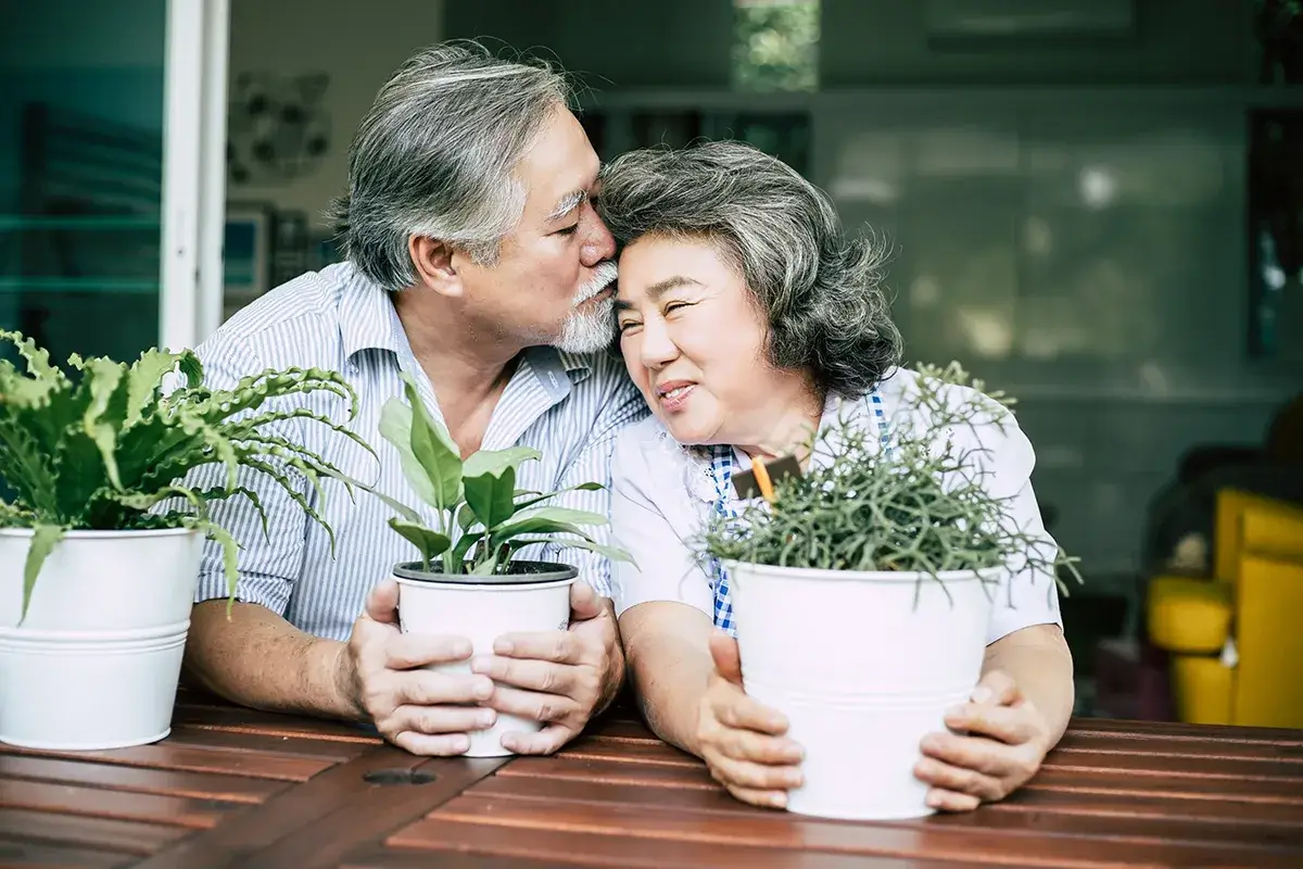 An older couple hugging while holding plants