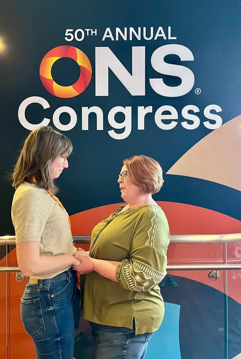 Traci and another speaker hugging in front of the 50th Annual ONS Congress logo